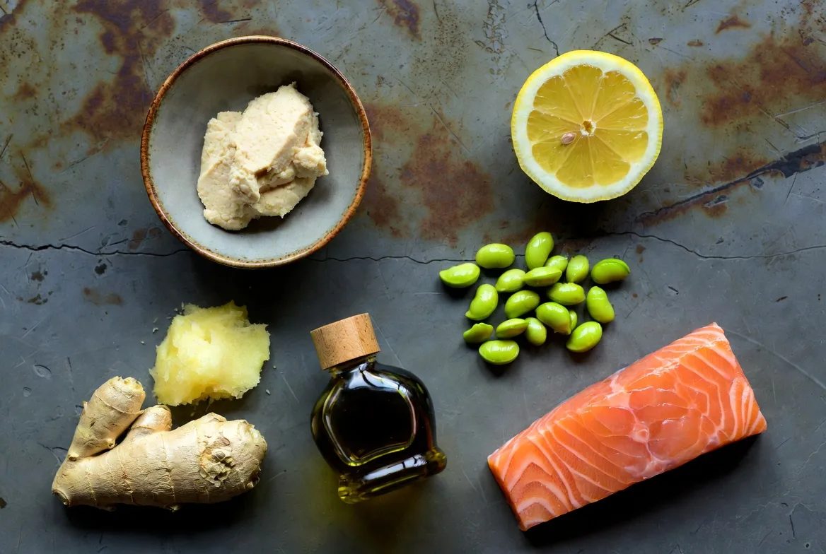 Fresh ingredients for miso glazed salmon bowl including raw salmon fillets, white miso paste, shelled edamame, and fresh ginger on a kitchen surface