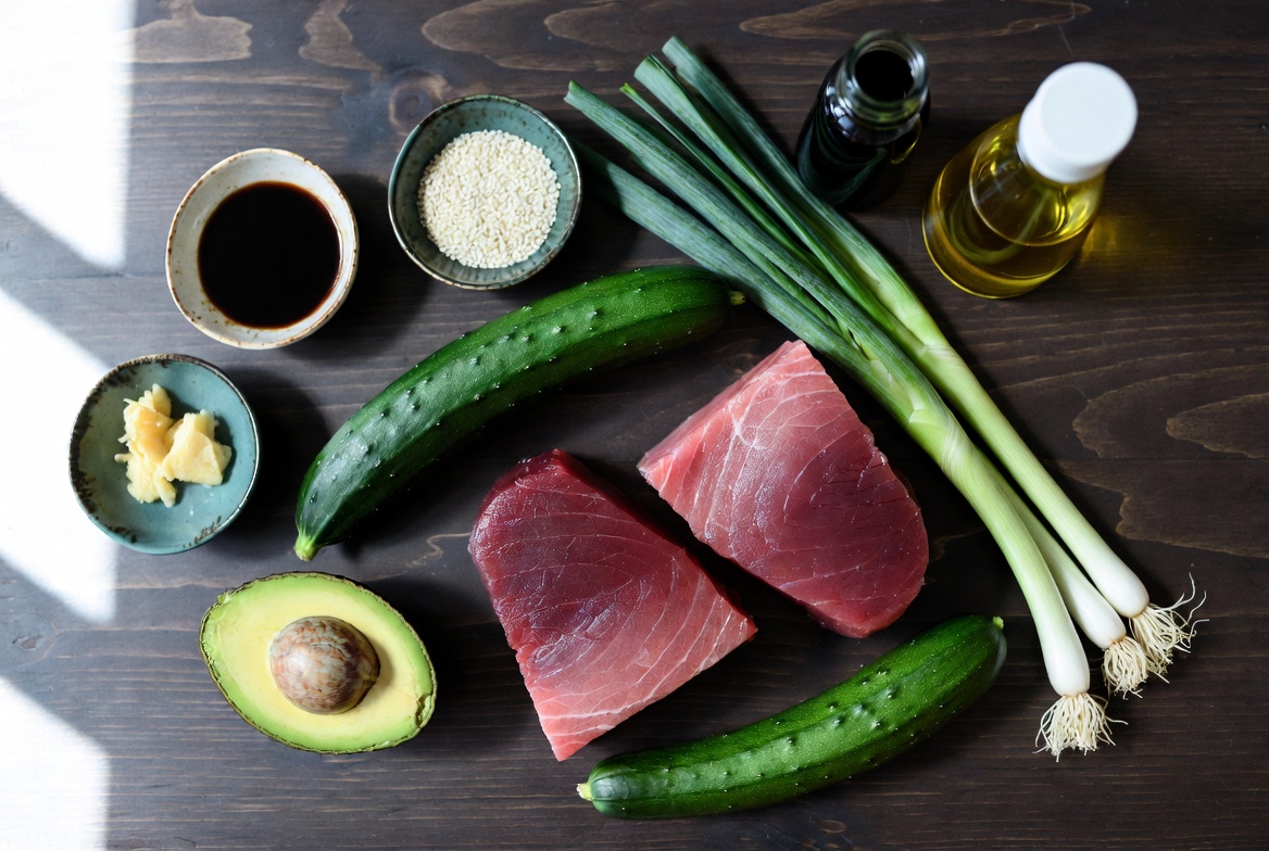 Fresh ingredients for seared tuna cucumber noodle bowl including tuna steaks, cucumber, avocado and sesame